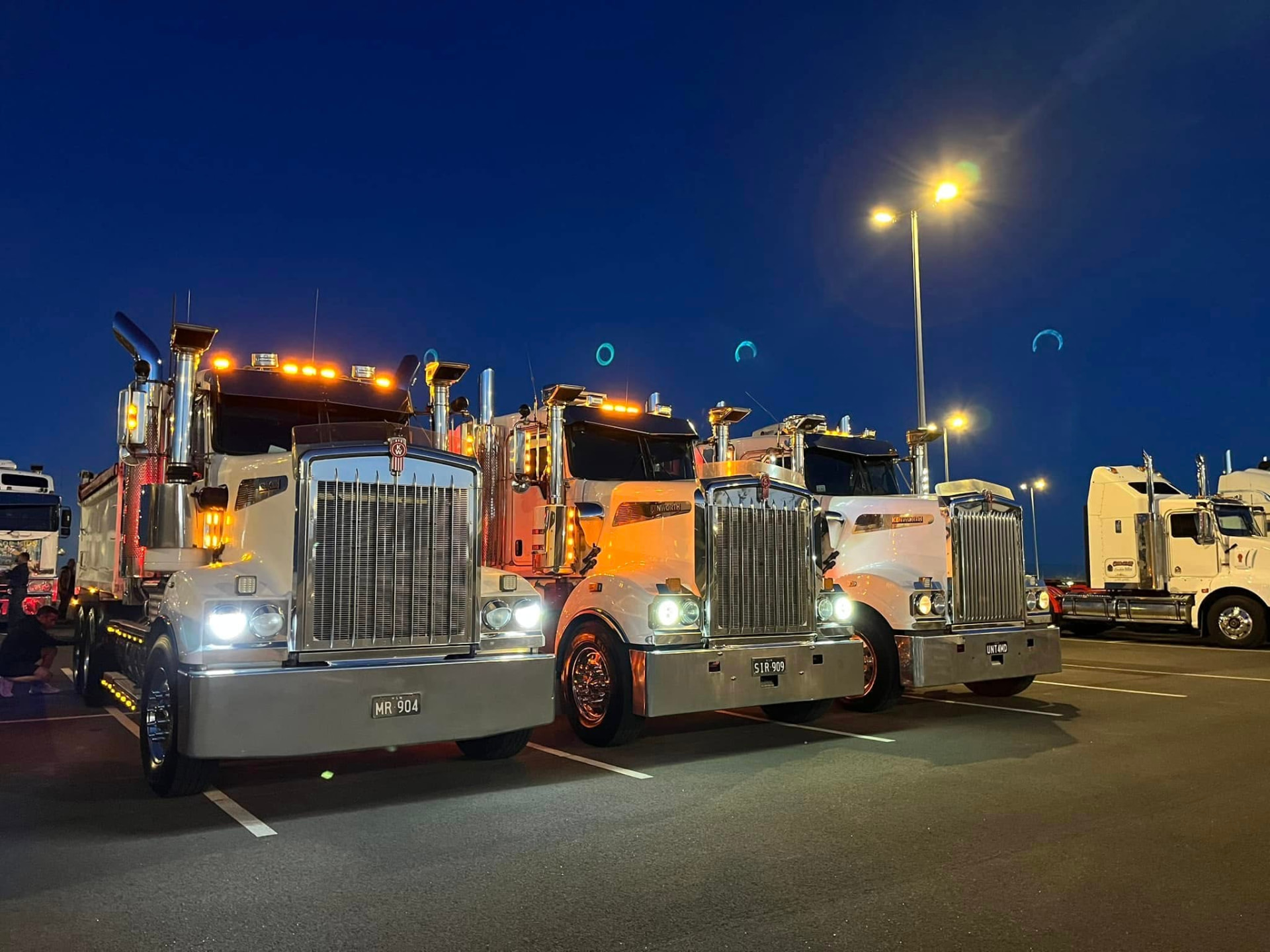 Three Hancock Excavations tipper trucks at the depot at night with their lights on